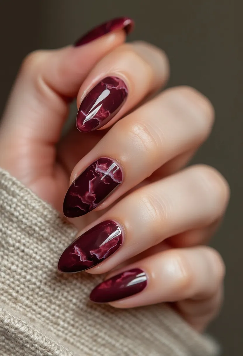 The nail design features a sophisticated and deep burgundy color palette that exudes elegance. The nails are medium length and shaped into a sleek almond form, offering a refined and elongated appearance. An intricate marble pattern in lighter pink is artistically integrated into the dark base, giving each nail a unique and luxurious look. The high-gloss finish suggests the use of gel treatment, adding to the overall smooth and polished texture. This design is rich and dramatic, ideal for the autumn or winter seasons, and can also make a striking choice for special occasions or evening events.