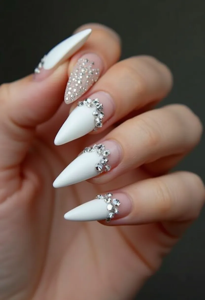 This nail design features a combination of white and clear colors, with a notable use of rhinestones for decoration. The nails are shaped into a stiletto form, which is elongated and pointed. Among the five nails, one showcases a full coverage of glitter, adding a sparkling effect to the design. The other nails are predominantly white with clear bases, adorned with clusters of rhinestones near the cuticles, creating a glamorous and eye-catching finish. The use of rhinestones and the overall aesthetic suggests a detailed and possibly gel-based nail treatment, making the design suitable for special occasions or events such as weddings or holiday celebrations.