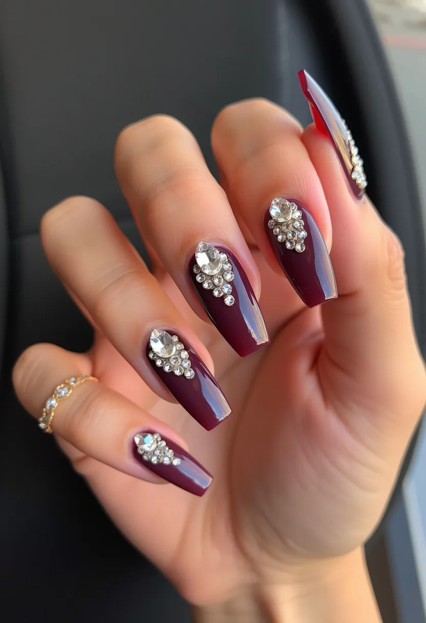 The nail design showcases a rich deep plum color palette with a glossy finish. The nails are long and shaped in a squared coffin style, providing a sophisticated and trendy look. Each nail is adorned with intricate decorations, featuring an array of rhinestones and gemstones that form elaborate patterns near the cuticle, adding a touch of glamour and elegance. This design appears to utilize gel treatment, ensuring a smooth and durable finish. The intricate gemstone pattern suggests it might be suitable for special occasions such as weddings or gala events, and the deep plum color evokes a seasonal fall or winter theme.