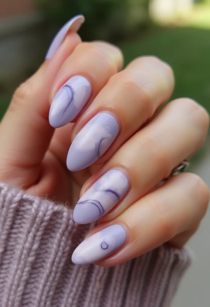 The nail design features a soothing lavender color palette, giving a soft and elegant appearance. The nails are shaped in an almond style, which complements the delicate aesthetic of the design. Each nail has a distinct yet cohesive pattern of light, swirling marble-like lines in deeper shades of lavender and purple, adding an intricate and artistic touch. The treatment appears to be gel nails, providing a glossy and long-lasting finish. This manicure could be ideal for spring, owing to its light and pastel tones, making it fitting for seasonal transitions or soft, elegant occasions. The integration of abstract line patterns makes the design unique and visually engaging.