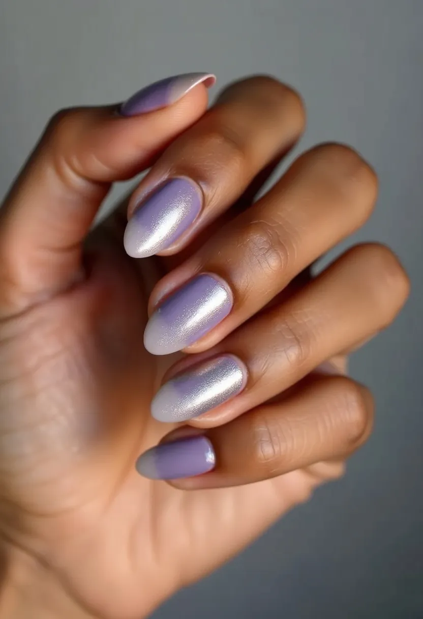 The nail design features an elegant and soft pastel color palette, predominantly showcasing shades of lavender and white with a pearlescent finish. The nails are shaped in a medium-length almond form, adding a sophisticated touch. The gradient effect on the nails creates a smooth transition from the lavender base to the white tips, giving a modern and polished look. This design appears to be achieved using gel polish, which enhances the glossy and durable finish. The subtle shimmer adds a hint of sparkle, making it suitable for both everyday wear and special occasions, potentially leaning towards a spring or summer theme due to its light and fresh colors.