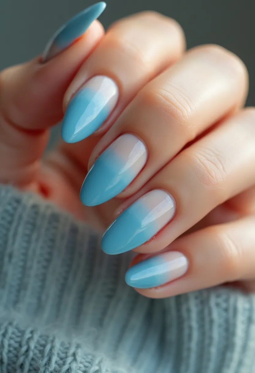 This nail design showcases a soft, pastel color palette predominantly featuring light blue and white hues. The nails are elegantly shaped in an almond form, gradually tapering to a subtle point. The design employs an ombré effect, blending the light blue seamlessly into the white towards the base of the nails, providing a smooth, gradient appearance. The nail treatment appears to be gel, given the glossy and smooth finish. This gentle color transition and the cool tones suggest a winter or spring theme, making it perfect for seasonal occasions or to complement a sophisticated, chic style.