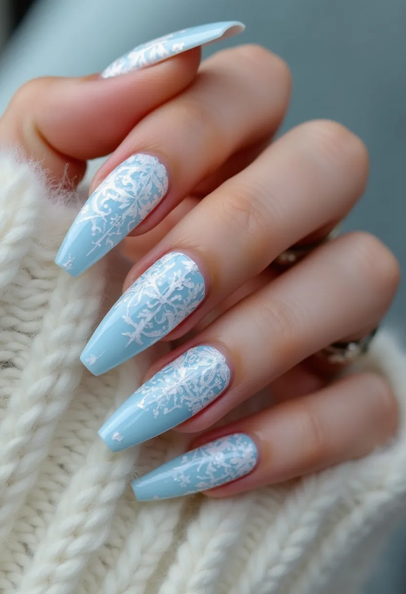 The nail design features a soft, pastel blue color palette, creating a tranquil and wintery look. The nails are long and tapered with a coffin shape, elegantly elongating the fingers. Intricate white patterns resembling delicate snowflakes are artfully painted on each nail, adding a festive and seasonal touch perfect for winter. The glossy finish suggests the use of gel or shellac treatment, providing a smooth and shiny surface that enhances the design's overall aesthetic. This design is ideal for celebrating the winter season or special occasions such as holiday parties.