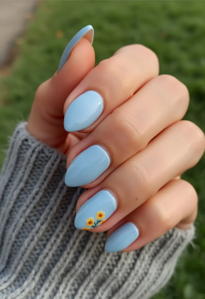 This nail design features a soft, pastel blue color palette applied to medium-length, almond-shaped nails, creating a fresh and elegant appearance. The nails appear to be finished with a gloss, indicating the use of either gel or shellac for a smooth and shiny surface. Adding a touch of intricate detail, one nail on each hand exhibits a delicate floral pattern with tiny sunflowers and green stems, enhancing the overall design with a hint of nature-inspired charm. The choice of blue and the sunflower decorations evoke a spring or summer theme, making this a perfect manicure for those seasons or light-hearted occasions. The meticulous attention to detail and precise execution of the floral patterns reflect a well-crafted and personalized nail treatment.