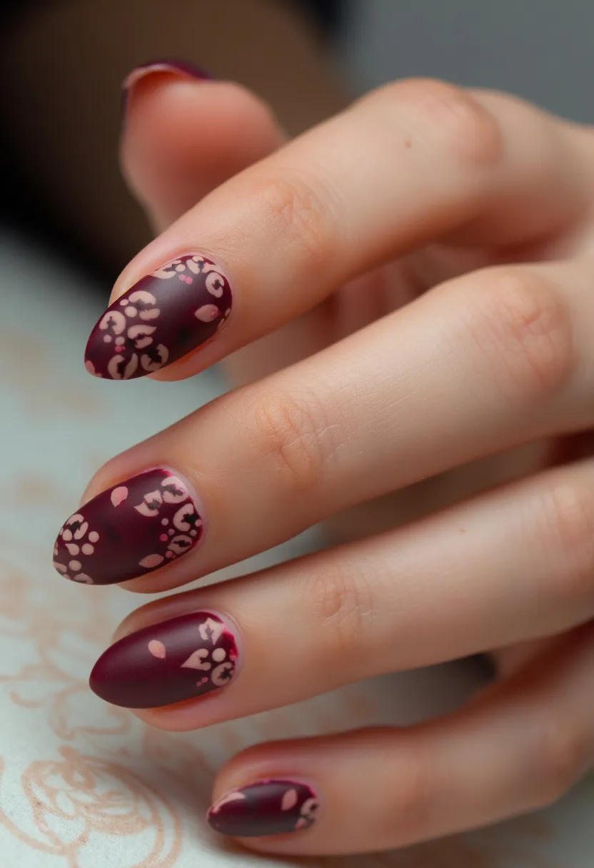 The nail design presents a sophisticated and artistic manicure featuring a deep maroon color palette adorned with intricate floral patterns. The nails are shaped in an elegant almond style, adding to the overall refined look. The floral motifs are subtly designed in a lighter shade of maroon or pinkish-brown, providing a delicate contrast against the darker base. The treatment appears to be a gel manicure, giving a smooth and glossy finish that enhances the rich color and details. This design exudes an autumnal theme, making it well-suited for the fall season or special occasions such as weddings or festive gatherings.