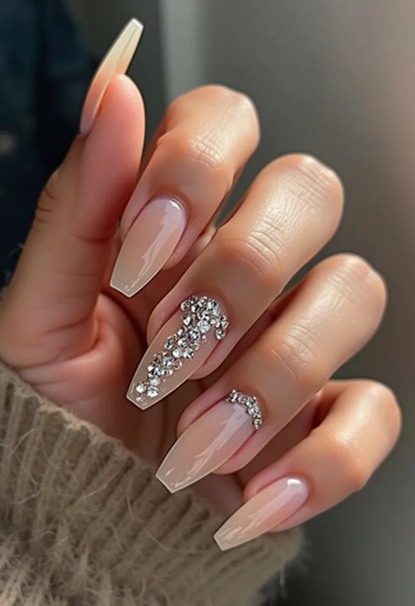 The nail design features a neutral, soft pink color palette, providing an elegant and understated base. The nails are shaped in an elongated square form, offering a sleek and sophisticated look. They appear to be treated with gel, lending a glossy and polished finish. The index and ring fingers are accentuated with intricate rhinestone decorations; the ring finger showcases a cluster of stones arranged in a cascading pattern, while the index finger sports a neat row of rhinestones near the cuticle. This design imbues a sense of glamour and could be suitable for formal events or special occasions, adding a touch of sparkle and sophistication.