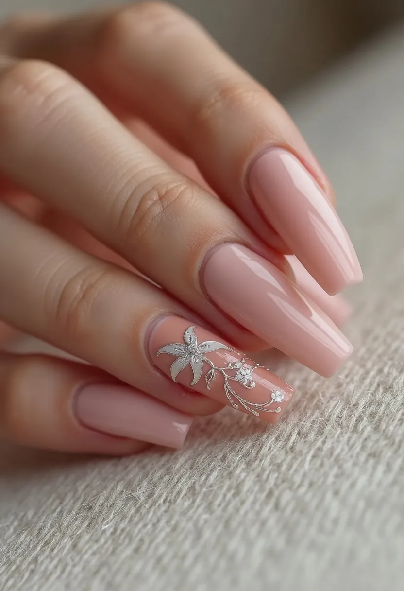 This nail design features long, elegantly shaped coffin nails with a soft pink color palette. The nails are likely treated with gel polish, giving them a glossy and smooth finish. One nail stands out with an intricate decoration, featuring a delicate floral pattern with a prominent silver flower and complementing smaller floral accents, adding a touch of sophistication and charm. The overall design exudes a subtle and refined aesthetic, making it suitable for various occasions, including weddings or formal events, while the floral detail hints at a spring or summer theme. The well-executed design showcases meticulous craftsmanship and attention to detail.