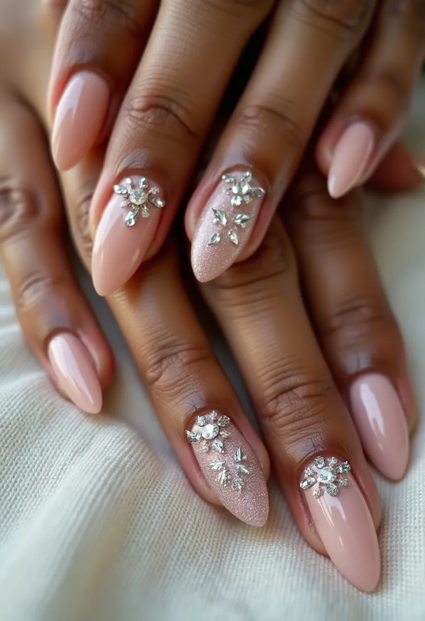 The nail design showcases a sophisticated and elegant look featuring a nude or soft pink color palette. The nails are shaped into an almond style, known for its modern and stylish appearance. This design incorporates a gel or possibly shellac treatment, providing a glossy, long-lasting finish. Intricate patterns adorn selected nails, specifically featuring delicate, sparkling rhinestone decorations that create floral or snowflake-like motifs, adding a touch of glamour. These features suggest a design suitable for a formal occasion, such as a wedding or an evening event. Each nail is meticulously crafted to blend simplicity with opulence, balancing the understated base color with strikingly detailed embellishments.